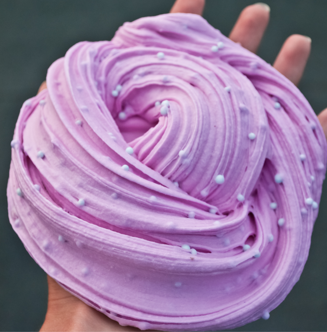 Close-up of swirled lilac butter slime dotted with small white beads, pressed with fingertips