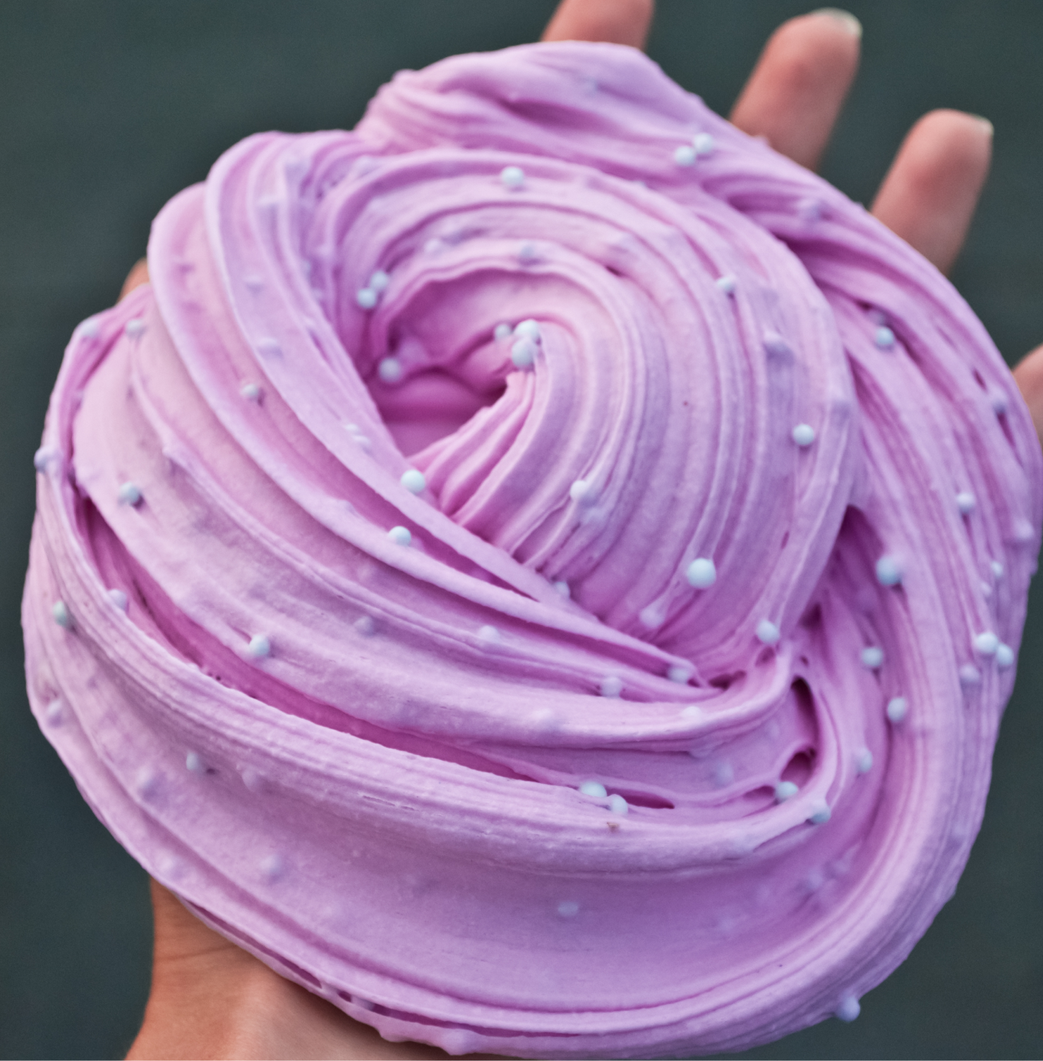 Close-up of swirled lilac butter slime dotted with small white beads, pressed with fingertips