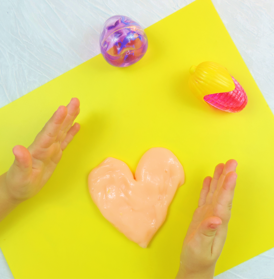 Overhead view of small clear slime pots in purple, yellow and pink arranged on bright yellow paper, ready as party gifts