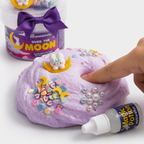 Finger pressing into lilac Over the Moon butter slime topped with pearly beads and a bunny-on-the-moon charm