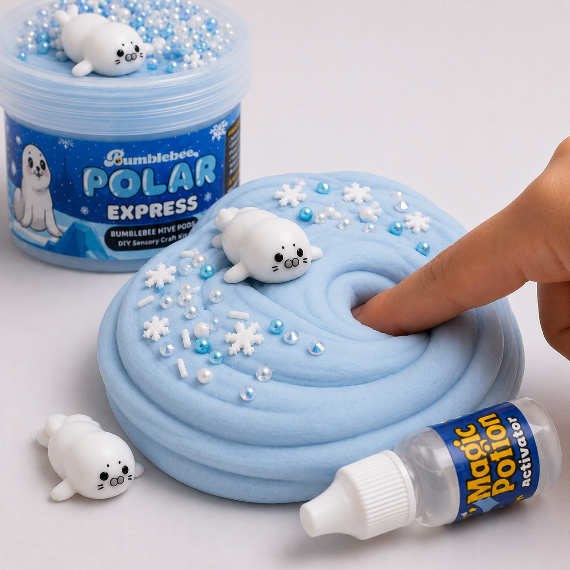 Finger pressing into pale blue Polar Express butter slime topped with snowflakes, pearl beads and a baby seal charm