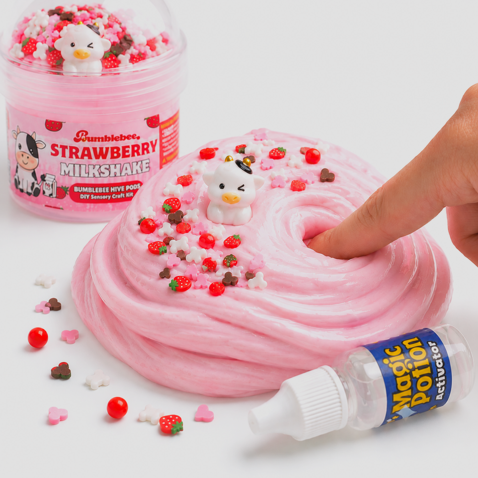 Finger pressing into baby pink Strawberry Milkshake slime topped with a cow charm and strawberry sprinkles